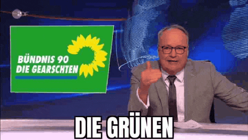 a man in a suit and tie is giving a thumbs up in front of a green sign that says die grünen