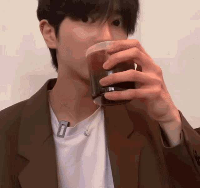 a man in a brown jacket is drinking from a cup with the letter p on it