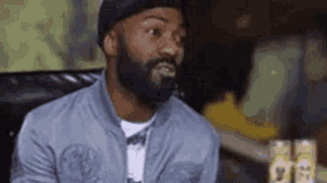 a man with a beard is sitting on a couch and looking at the camera .