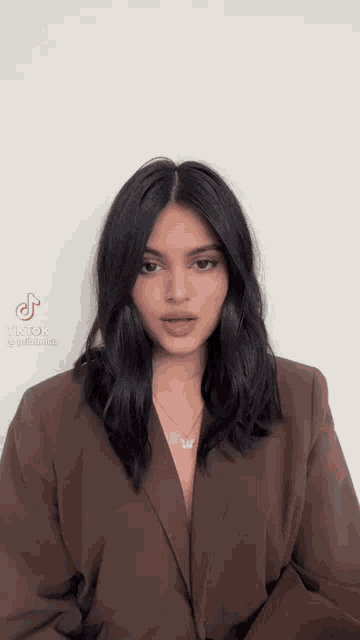 a woman with dark hair is wearing a brown jacket and a necklace