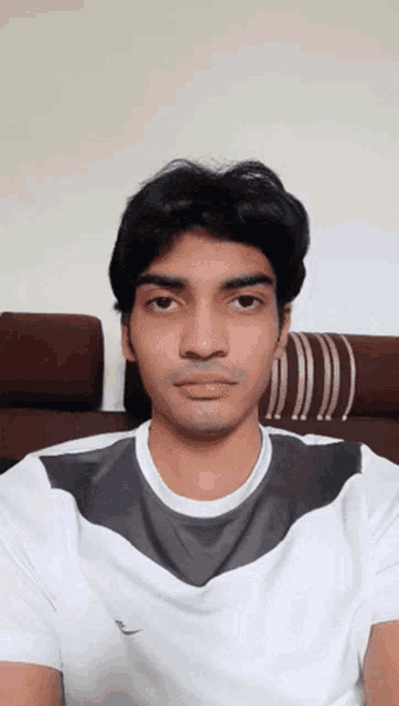 a young man wearing a white t-shirt with a gray collar looks at the camera