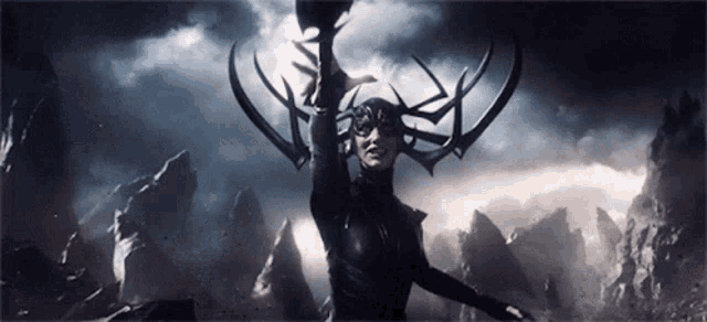 a woman with horns on her head is holding a sword in front of a mountain range .