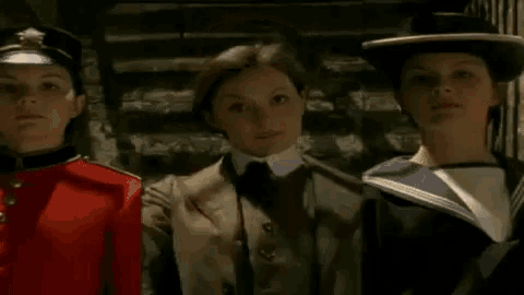three young girls wearing hats and uniforms are standing next to each other in a dark room .