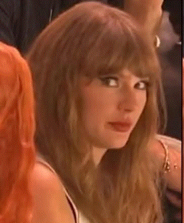 a woman with long brown hair and bangs is sitting in a crowd of people and looking at the camera .