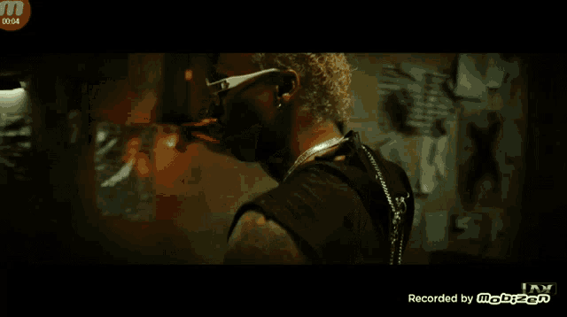a man wearing sunglasses is standing in a dark room and the time is 10:05