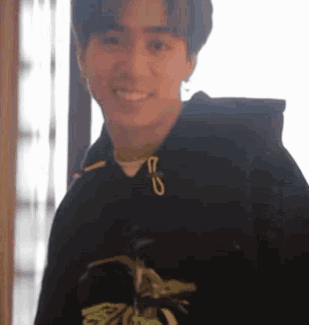 a young man wearing a black hoodie is smiling while holding a bird in his hand .