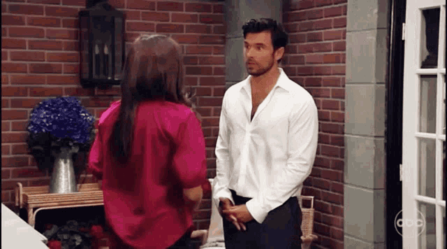 a man in a white shirt is standing next to a woman in a pink shirt in front of a brick wall