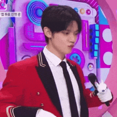 a young man in a red suit and tie is holding a microphone and a stuffed animal .