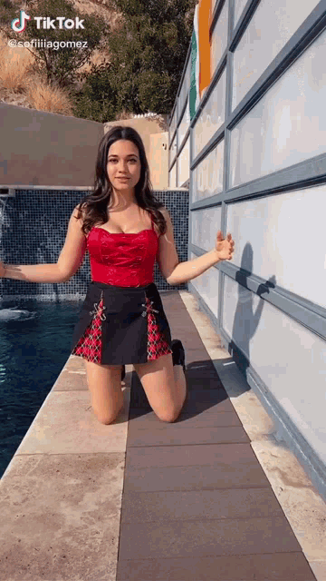 a woman in a red top and a black skirt is kneeling on the sidewalk next to a pool .