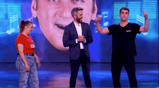 two men and a woman are dancing on a stage in front of a man 's face ..
