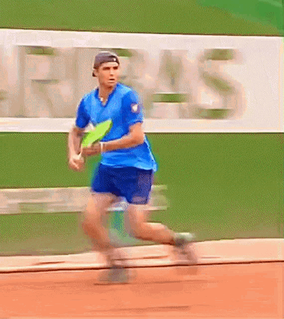 a man in a blue shirt is running on a tennis court holding a tennis racket .