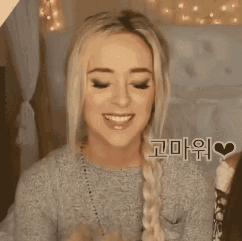 a woman with blonde hair and a braid is smiling while wearing a grey sweater .