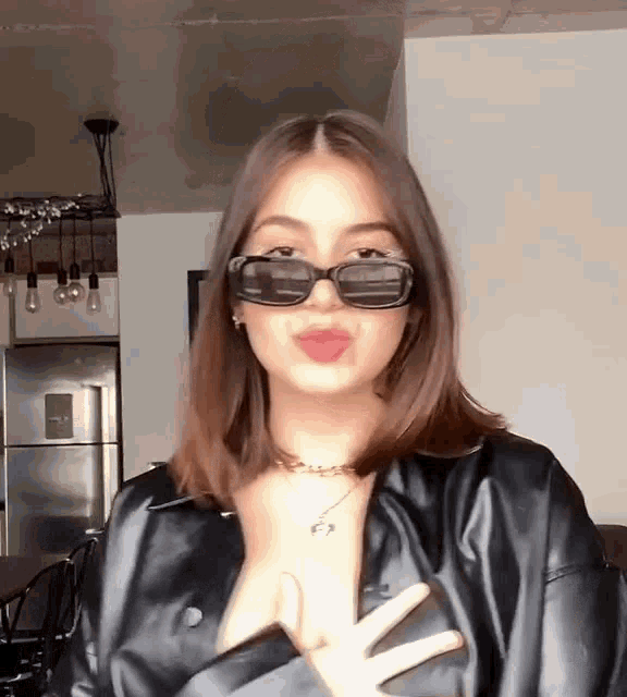 a woman wearing sunglasses and a black leather jacket is giving a kiss .