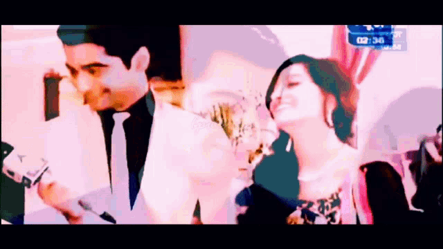 a man in a suit and tie stands next to a woman in a pink dress and a clock that reads 02:36