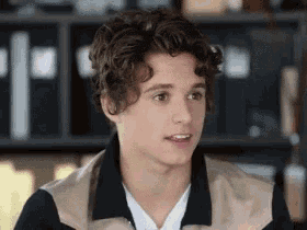 a young man with curly hair is wearing a jacket and a white shirt and looking at the camera .