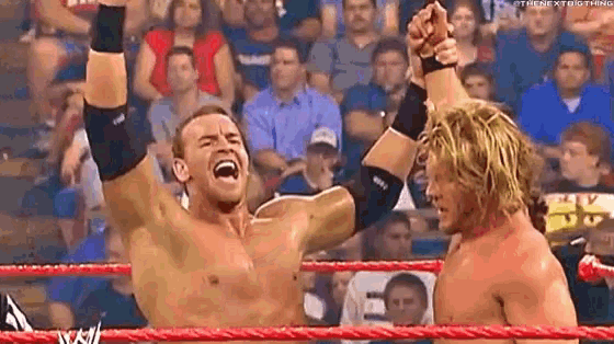 two wrestlers are standing in a wrestling ring with their hands in the air .
