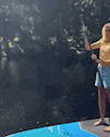 a couple of people standing on top of a blue surfboard in front of a pool .