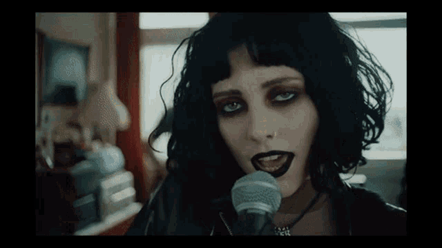 a woman singing into a microphone with black lipstick