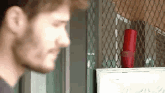 a man is standing in front of a fence with a red bottle in front of him .