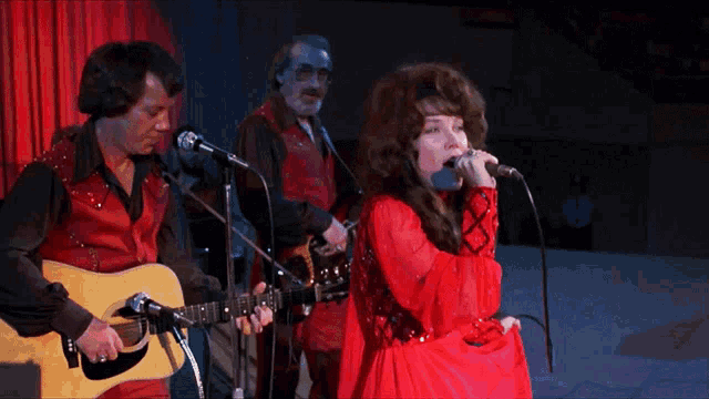 a woman in a red dress sings into a microphone while a man plays guitar