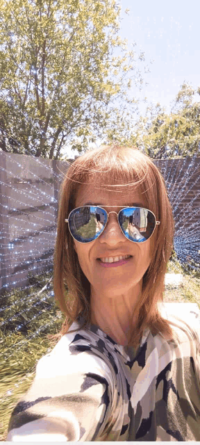 a woman wearing sunglasses takes a selfie in front of a fence