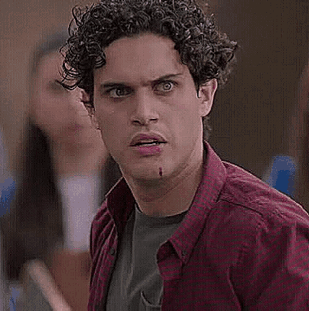 a man with curly hair is wearing a plaid shirt and a green shirt and has blood on his face .
