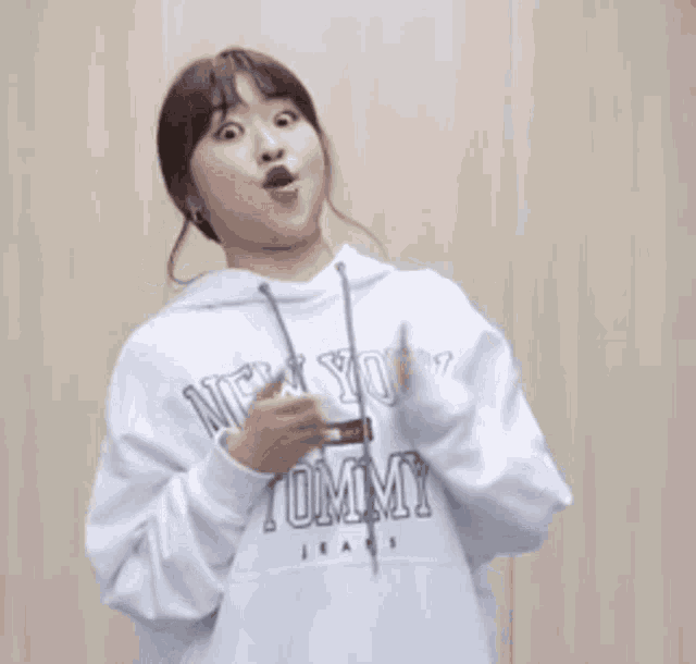 a woman is wearing a white tommy jeans hoodie and making a funny face .