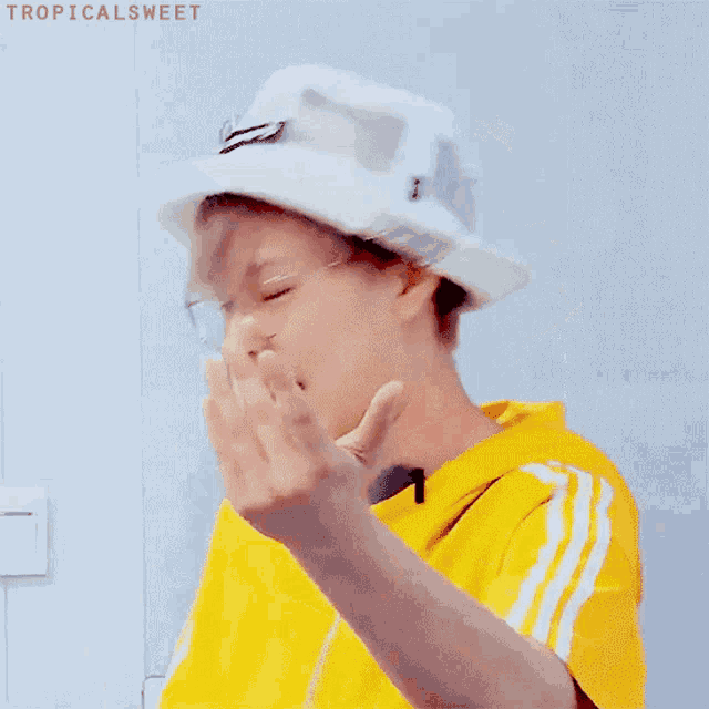 a person wearing a yellow shirt and a white hat with the word tropicalsweet written on the bottom