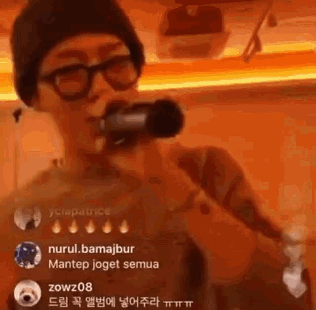 a man is singing into a microphone while wearing glasses and a hat .