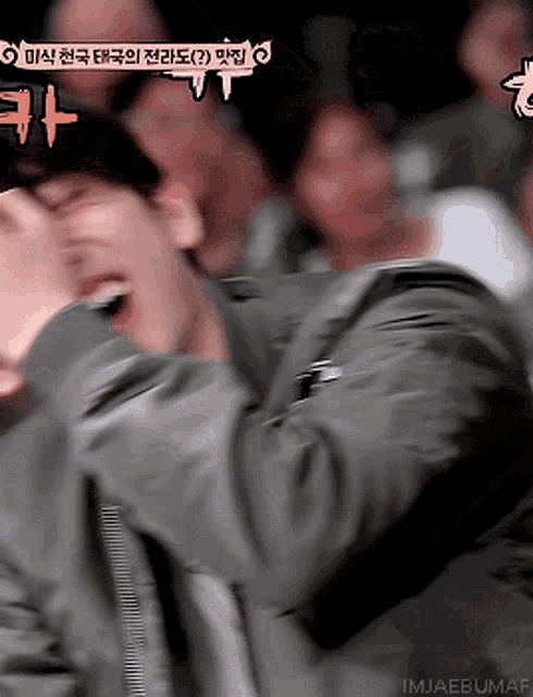 a man is laughing in front of a crowd with a sign that says imjaebumaf on it