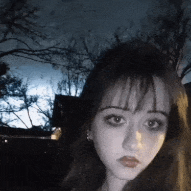a young girl with dark hair is taking a selfie in front of a house .