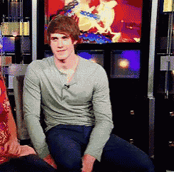 a man in a grey shirt is sitting in front of a tv