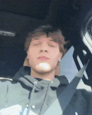 a young man in a hoodie is sitting in a car with his eyes closed
