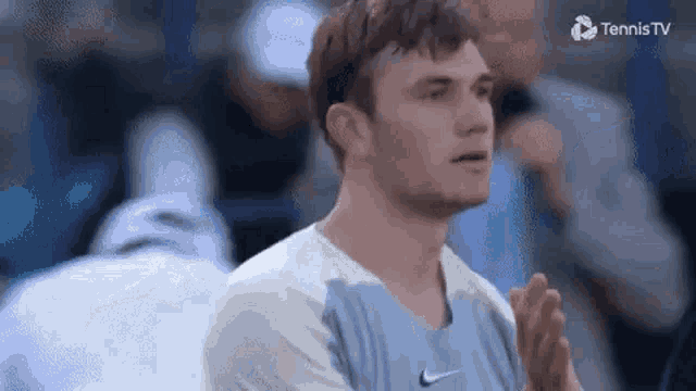 a man in a blue and white nike shirt is clapping his hands while standing on a tennis court .