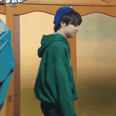 a boy wearing a green hoodie and a blue beanie is standing in front of a door that says the world