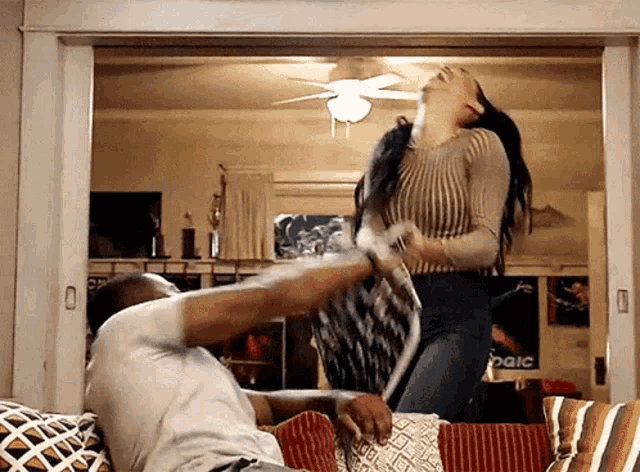 a man and a woman are having a pillow fight in a living room with a peace sign in the background