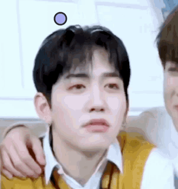 a young man with a circle on his head is making a funny face while being hugged by another young man .