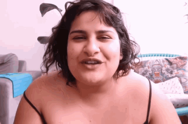 a woman in a black tank top is smiling and making a funny face .