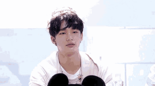 a young man wearing a white sweater and a mickey mouse headband is sitting down and looking at the camera .