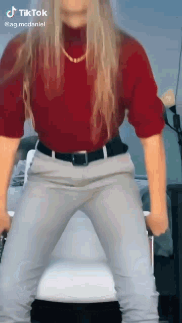 a woman in a red turtleneck and grey pants is dancing on a tiktok video