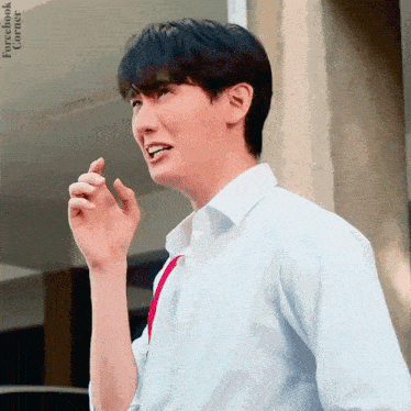 a young man in a white shirt and red tie is standing in front of a building and talking on a cell phone .