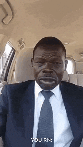 a man in a suit and tie is sitting in a car and making a funny face .