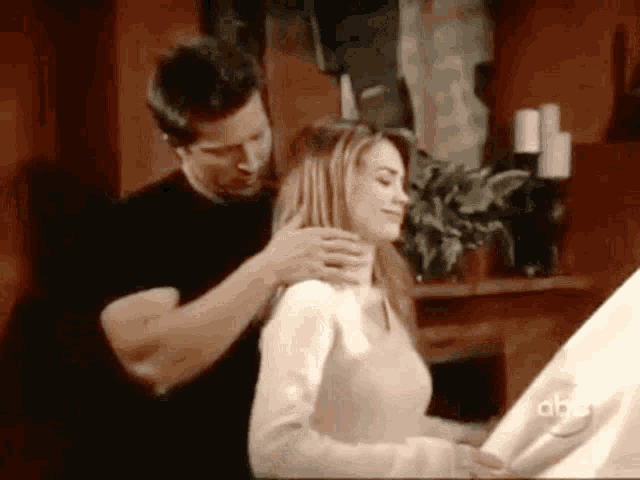 a man is putting his hand on a woman 's neck while she sits at a table