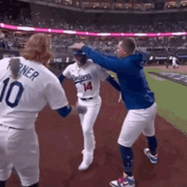 a baseball player with the number 14 on his jersey is being greeted by two other players .
