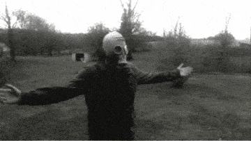 a person wearing a gas mask stands in a field with their arms outstretched