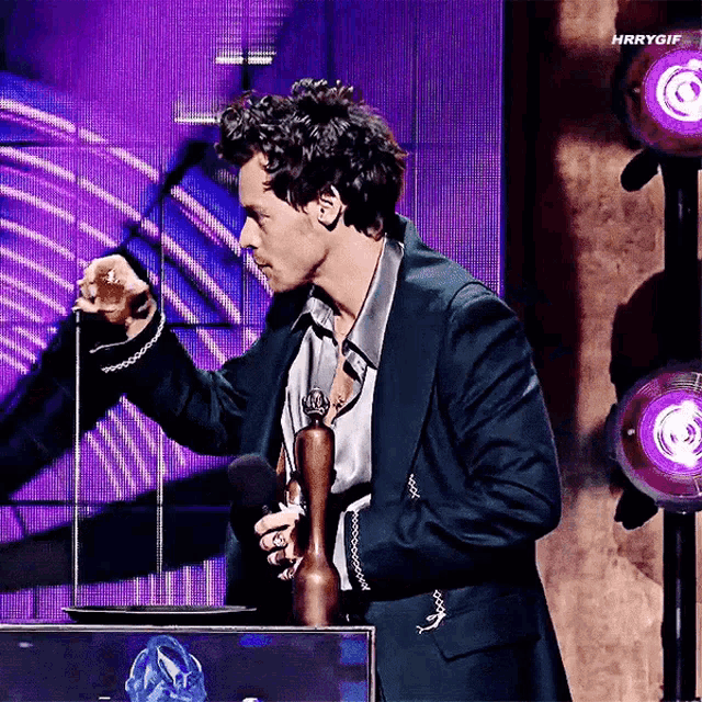 a man in a suit is holding a microphone and a trophy .