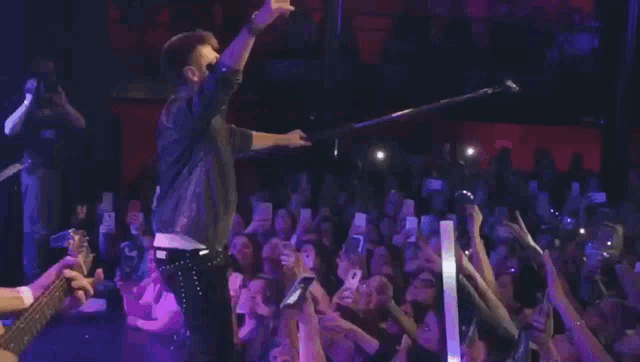 a man singing into a microphone in front of a crowd that is holding up their cell phones