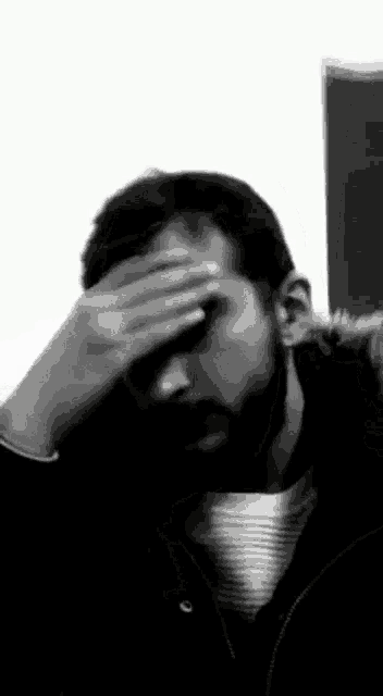 a man with a beard is covering his face with his hands .