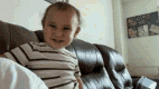a baby is sitting on a couch looking at the camera and smiling .