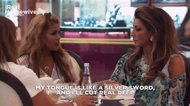 two women sitting at a table with a real housewives logo on the bottom right